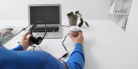 Female hands with headphones, modern laptop and cup of coffee at white table