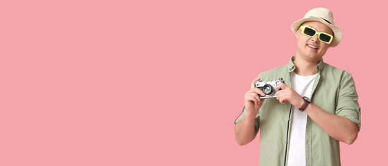Young male tourist with photo camera on pink background
