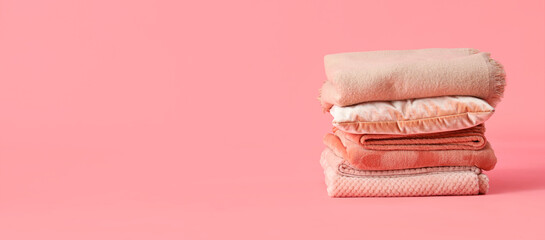 Stack of folded warm plaids and pillow on pink background
