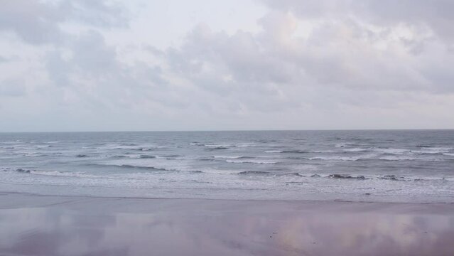 4K aerial view of ocean waves crashing on beach shore during cloudy day at Mandvi, Kutch, India. Calm coastline with sandy beach. Summer vacation, beach holidays concept. Travel and tourism background