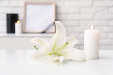 Burning candle and beautiful lily flower on light table in room