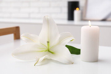 Burning candle and beautiful lily flower on light table in room