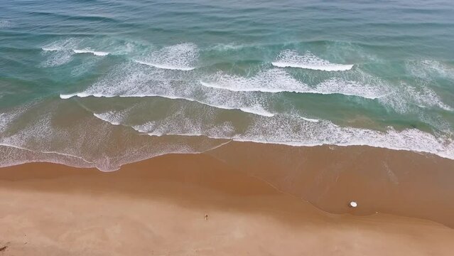 Praia quase vazia e surfistas no mar azul no litoral do nordeste brasileiro. Drone filmando de cima surfistas pequenos na amplitude do mar em Taipu de Fora, Bahia, Brasil