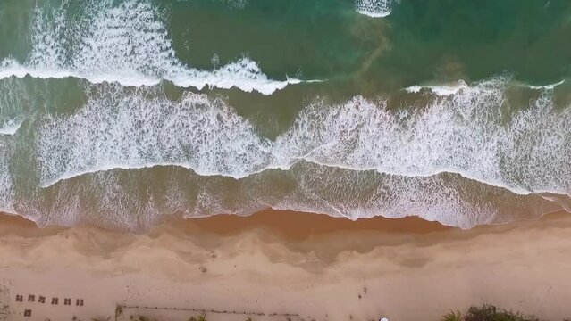 Drone fixo no ar filmando de cima as ondas quebrando em praia deserta brasileira