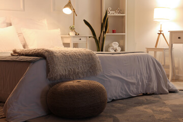 Soft blanket on bed and wicker pouf in cozy bedroom at night