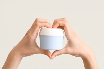 Female hands in shape of heart with jar of cream on light background, closeup