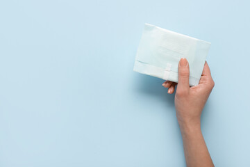 Female hand with menstrual pad on blue background