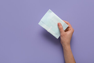 Female hand with menstrual pad on purple background