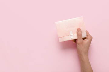 Female hand with menstrual pad on pink background