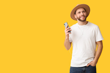 Happy young man in modern earphones with mobile phone on yellow background