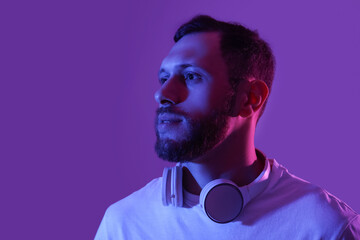Young man in modern headphones on purple background