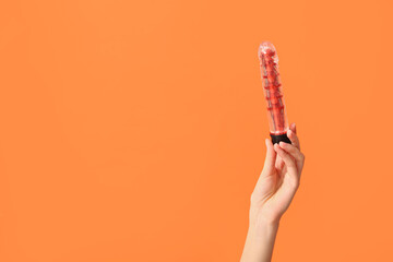 Female hand with vibrator on orange background, closeup