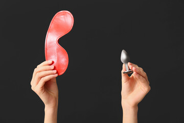 Female hands with mask from sex shop and anal plug on dark background, closeup
