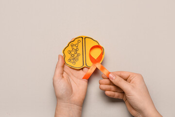 Female hands with paper brain and orange ribbon on grey background. Multiple Sclerosis Awareness...