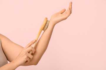 Young woman massaging her arm with body massage brush on pink background