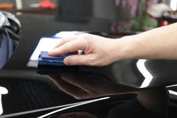 Car service worker applying nano coating on a car detail close-up. Closeup of hand coating black...