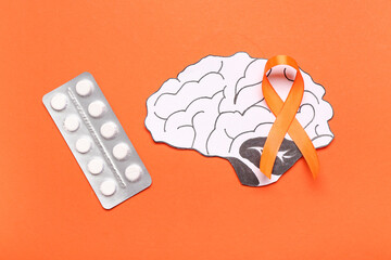 Paper brain with pills and orange ribbon on color background. Multiple Sclerosis Awareness Month