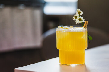 A refreshing glass of orange juice with ice, garnished with a sprig of mint and chamomile flowers,...