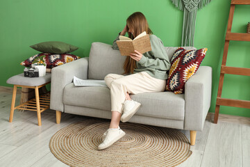 Obraz premium Young woman reading book on sofa in green living room