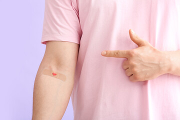 Blood donor pointing at applied medical patch on lilac background, closeup