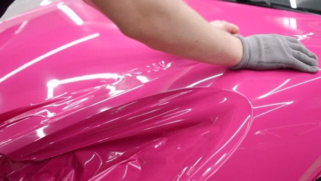A specialist in wrapping a car with pink-colored vinyl film in the process of work. Car wrapping specialists cover the car with vinyl sheet or film. Car wrapping close-up. Selective focus.