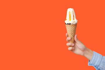 Female hand with sweet ice-cream in waffle cone on orange background