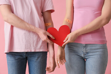 Blood donors with applied patches and paper heart on pink background, closeup