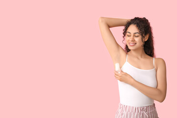 Beautiful young African-American woman applying deodorant on pink background