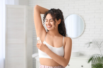 Beautiful young African-American woman applying deodorant in bathroom
