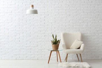 Armchair with cushion, houseplant and rug near brick white wall