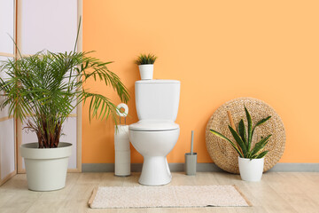 Interior of restroom with toilet bowl and plants near beige wall