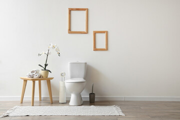 Interior of restroom with toilet bowl and coffee table with orchid and towels near white wall - Powered by Adobe