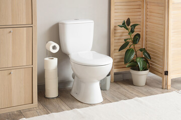 Interior of restroom with toilet bowl, plant and paper holder near grey wall