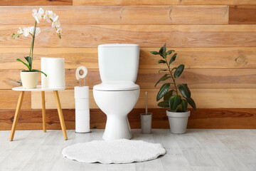 Interior of restroom with toilet bowl, coffee table with orchid and houseplant near wooden wall