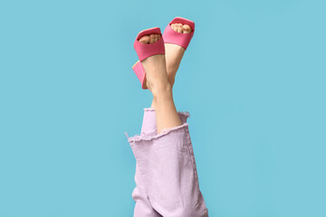 Legs of young woman in jeans and pink open-toed high heels on blue background
