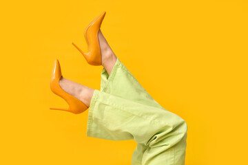 Legs of young woman in green jeans and high-heeled shoes on yellow background