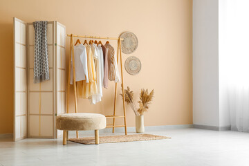 Rack with clothes, folding screen and pouf in dressing room