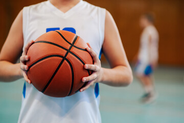 Cropped picture of junior basketball player holding a ball on court.
