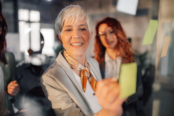 Senior businesswoman writing tasks and ideas on sticky notes at office.