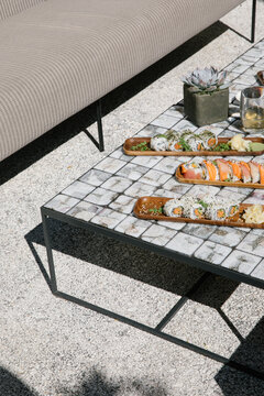 Three trays of sushi served on wooden plates on a table outdoors in the afternoon.