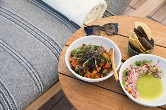 Ceviche, tortilla chips, and grain bowl with sweet potato next to a pool side lounge with sunglasses.
