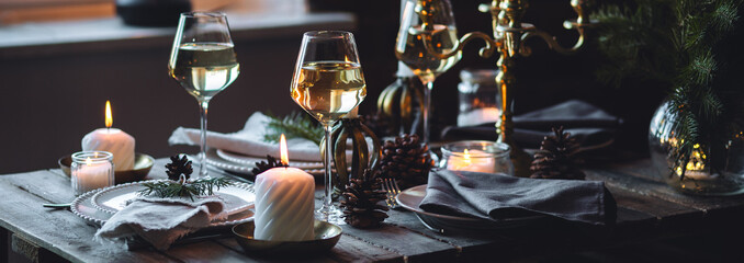 Banner. Beautiful table setting for family Christmas dinner at home. Cozy atmosphere, candlelight. Wine glasses, vintage chandelier, elegant interior. Fir tree branches, wooden furniture, dark, bokeh