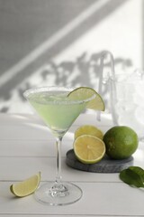 Delicious Margarita cocktail in glass and limes on white wooden table