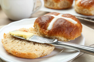 Tasty hot cross bun and knife with butter on table, closeup