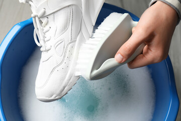 Woman cleaning stylish sneakers with brush in wash basin, top view