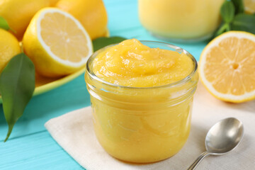 Delicious lemon curd in glass jar, fresh citrus fruits and spoon on light blue wooden table, closeup