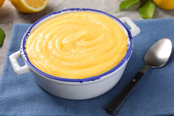 Delicious lemon curd in bowl and spoon on table, closeup