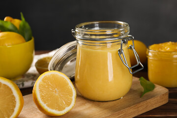 Delicious lemon curd in glass jars, fresh citrus fruits and green leaves on wooden table