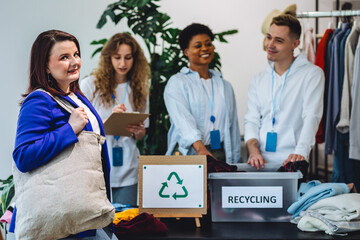 Group of volunteers, young women and man, sorting clothes in charitable foundation for charity donation, recycling. Concept of textile pollution, conscious consumption. Ecology, sustainable lifestyle