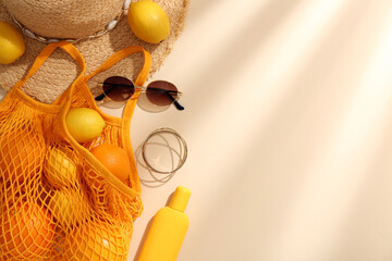 String bag with sunglasses, fruits and summer accessories on beige background, flat lay. Space for...